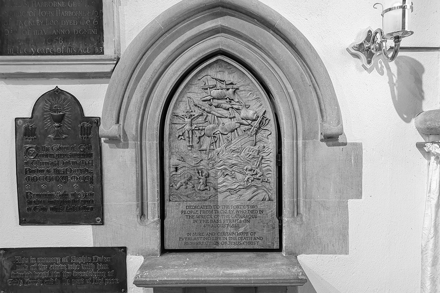 Carved wooden plaque in a stone Gothic alcove, with etched text and a relief depicting the disaster.