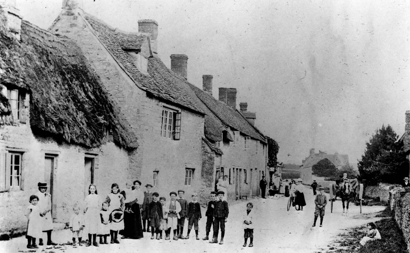 Old black-and-white photo. A crowd of people, mostly children, gather in the street for the camera.