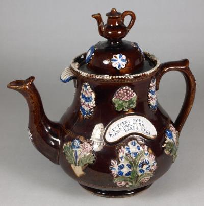 Ornate ceramic teapot painted brown and glazed. The lid handle is a miniature of the teapot itself.