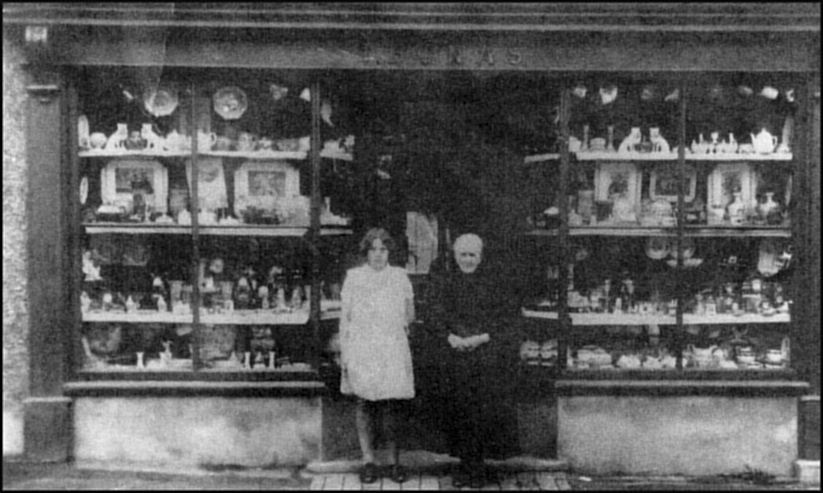 A woman and man stand in the doorway of a shop with window displays either side.