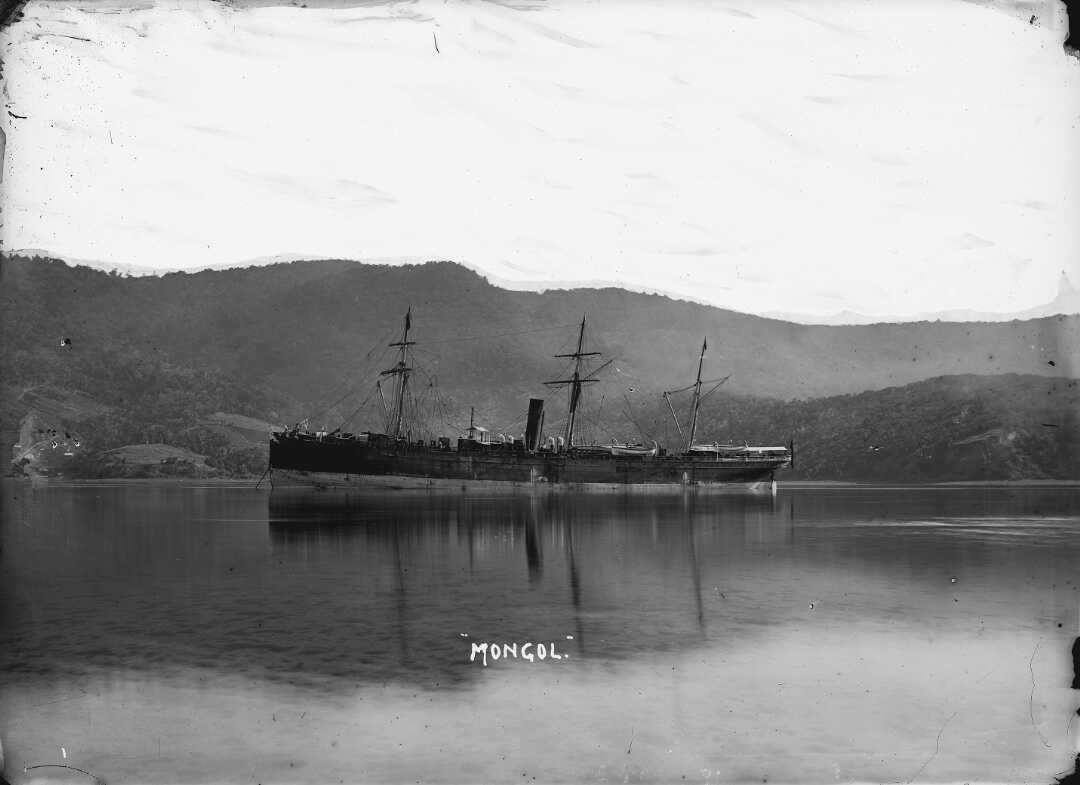 Long steamship on calm water with forested hills in the distance.